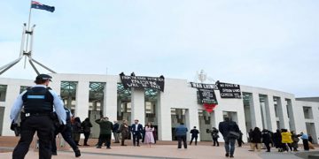 Personas solidarias con la lucha palestina izan carteles y banderas encima del Parlamento de Australia